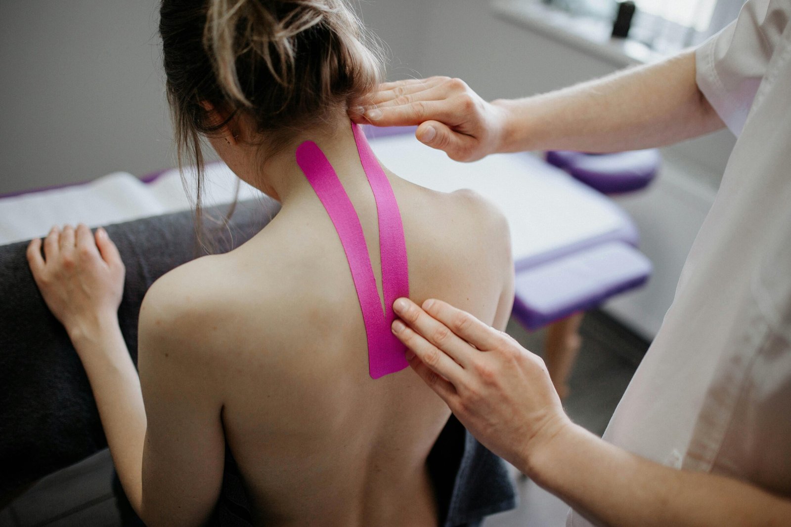 A healthcare professional applies kinesiology tape on a woman's neck for therapeutic treatment.